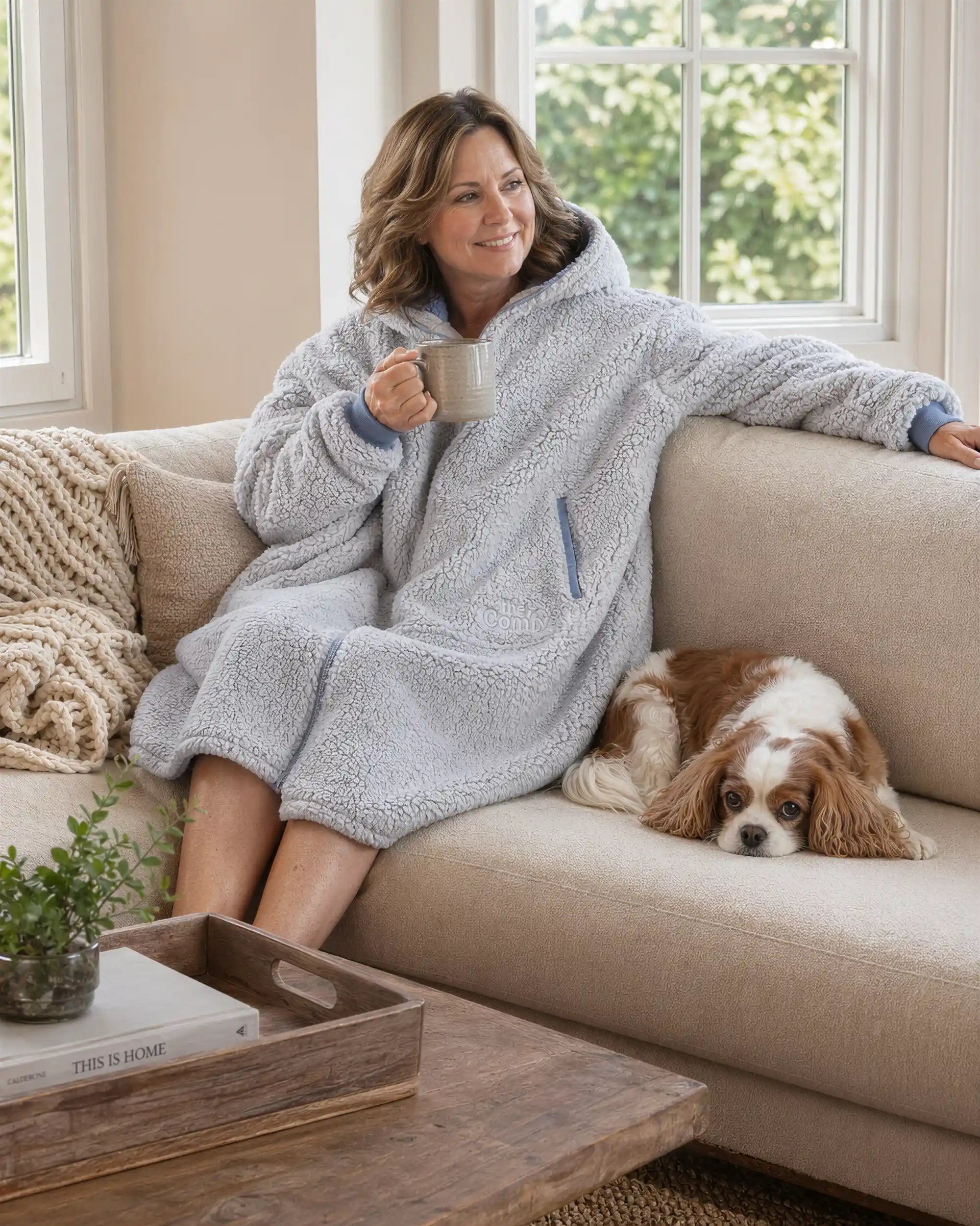 Woman relaxing on a couch in the Teddy Bear Full-Zip worn on the Light Gray side, enjoying cozy comfort with a warm drink and a quiet moment at home.