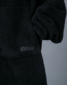 Close-up of The Teddy Bear Quarter-Zip wearable blanket in black showing sleeve detail and embroidered logo on CloudSherpa™ fabric