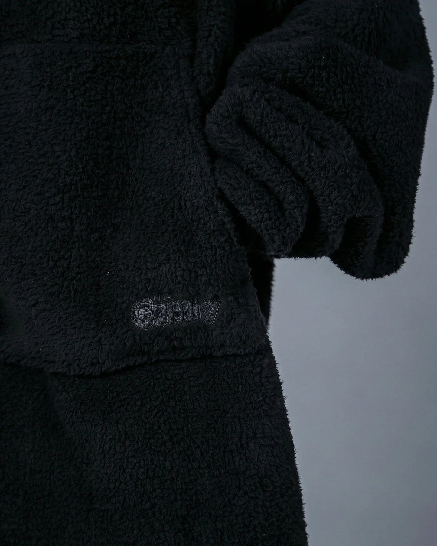 Close-up of The Teddy Bear Quarter-Zip wearable blanket in black showing sleeve detail and embroidered logo on CloudSherpa™ fabric