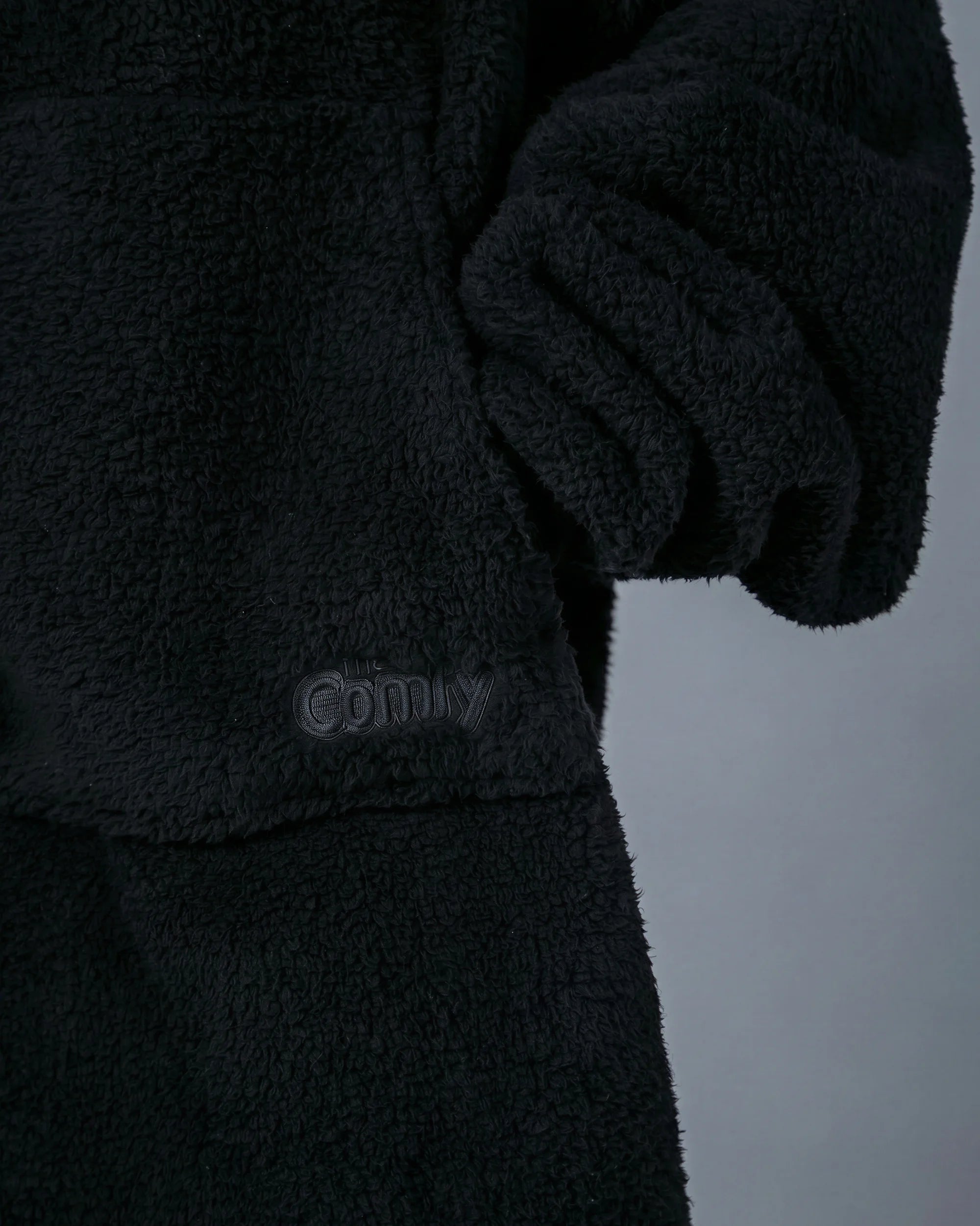 Close-up of The Teddy Bear Quarter-Zip wearable blanket in black showing sleeve detail and embroidered logo on CloudSherpa™ fabric