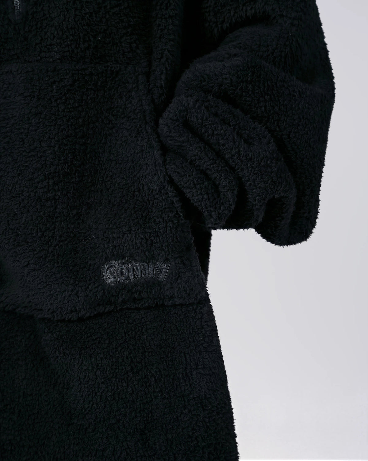 Close-up of The Teddy Bear Quarter-Zip wearable blanket in black showing sleeve detail and embroidered logo on CloudSherpa™ fabric
