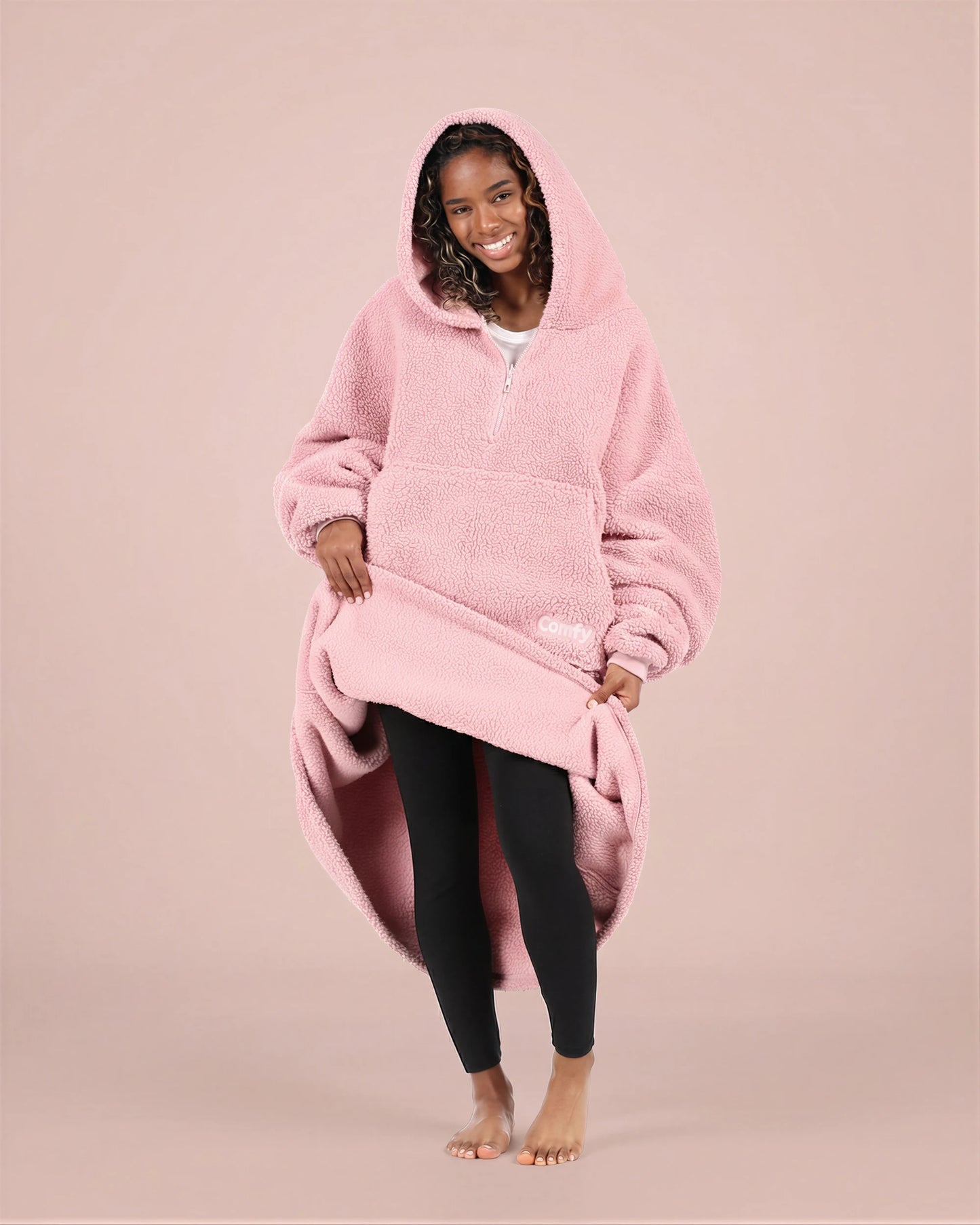 Front view of The Teddy Bear Quarter-Zip wearable blanket in blush with model lifting hem to show full coverage and soft interior