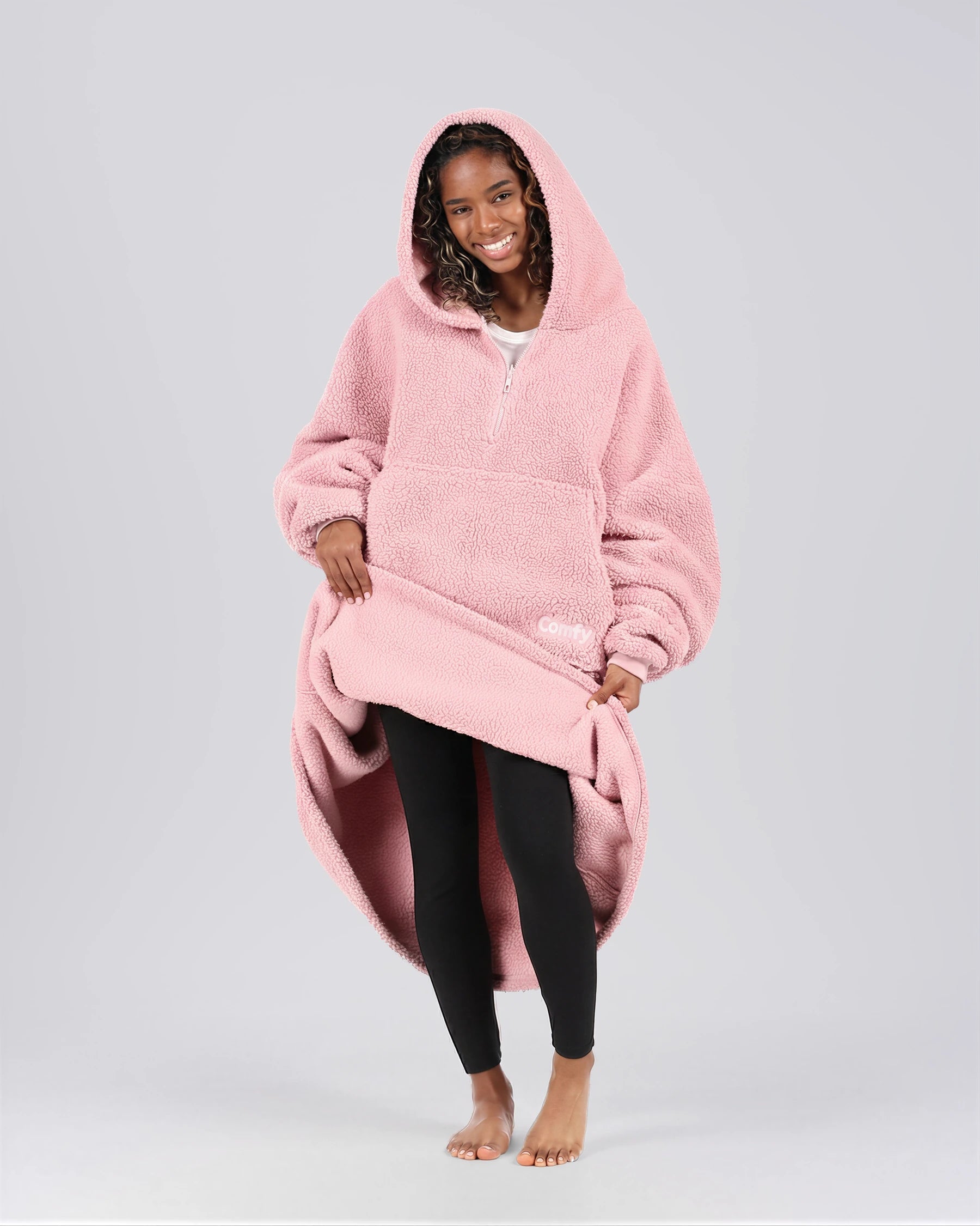 Front view of The Teddy Bear Quarter-Zip wearable blanket in blush with model lifting hem to show full coverage and soft interior