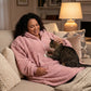 Lifestyle view of The Teddy Bear Quarter-Zip wearable blanket in blush worn lounging on a couch with a cat, showing cozy at-home use