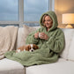Lifestyle view of The Teddy Bear Quarter-Zip wearable blanket in cucumber worn lounging on a couch with a dog, holding a mug, showing cozy at-home use
