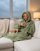 Lifestyle view of The Teddy Bear Quarter-Zip wearable blanket in cucumber worn lounging on a couch with a dog, holding a mug, showing cozy at-home use