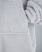 Close-up of The Teddy Bear Quarter-Zip wearable blanket in light gray showing embroidered logo and soft CloudSherpa™ texture