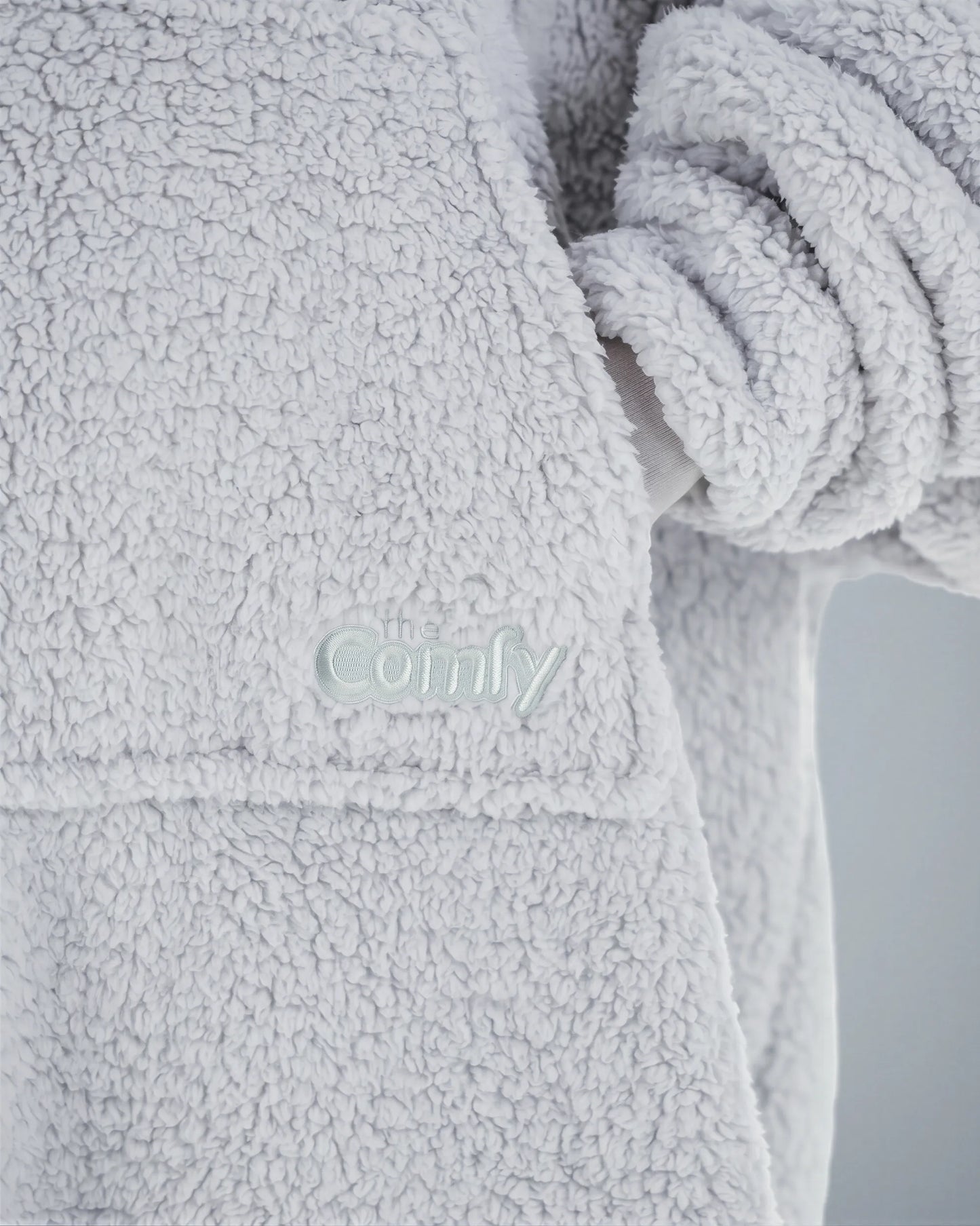 Close-up of The Teddy Bear Quarter-Zip wearable blanket in light gray showing embroidered logo and soft CloudSherpa™ texture