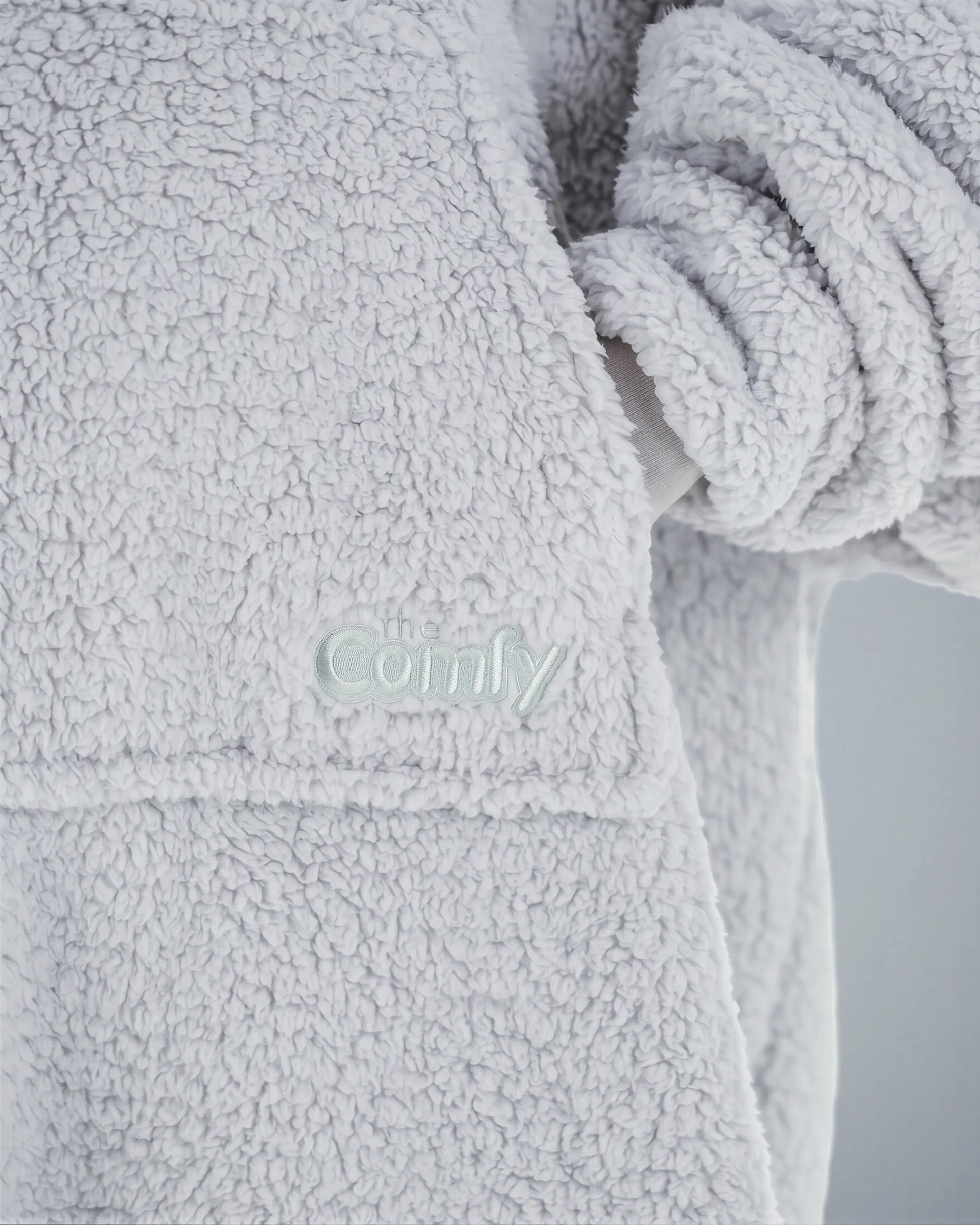 Close-up of The Teddy Bear Quarter-Zip wearable blanket in light gray showing embroidered logo and soft CloudSherpa™ texture
