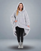 Front view of The Teddy Bear Quarter-Zip wearable blanket in light gray with model lifting hem to show full coverage and plush interior