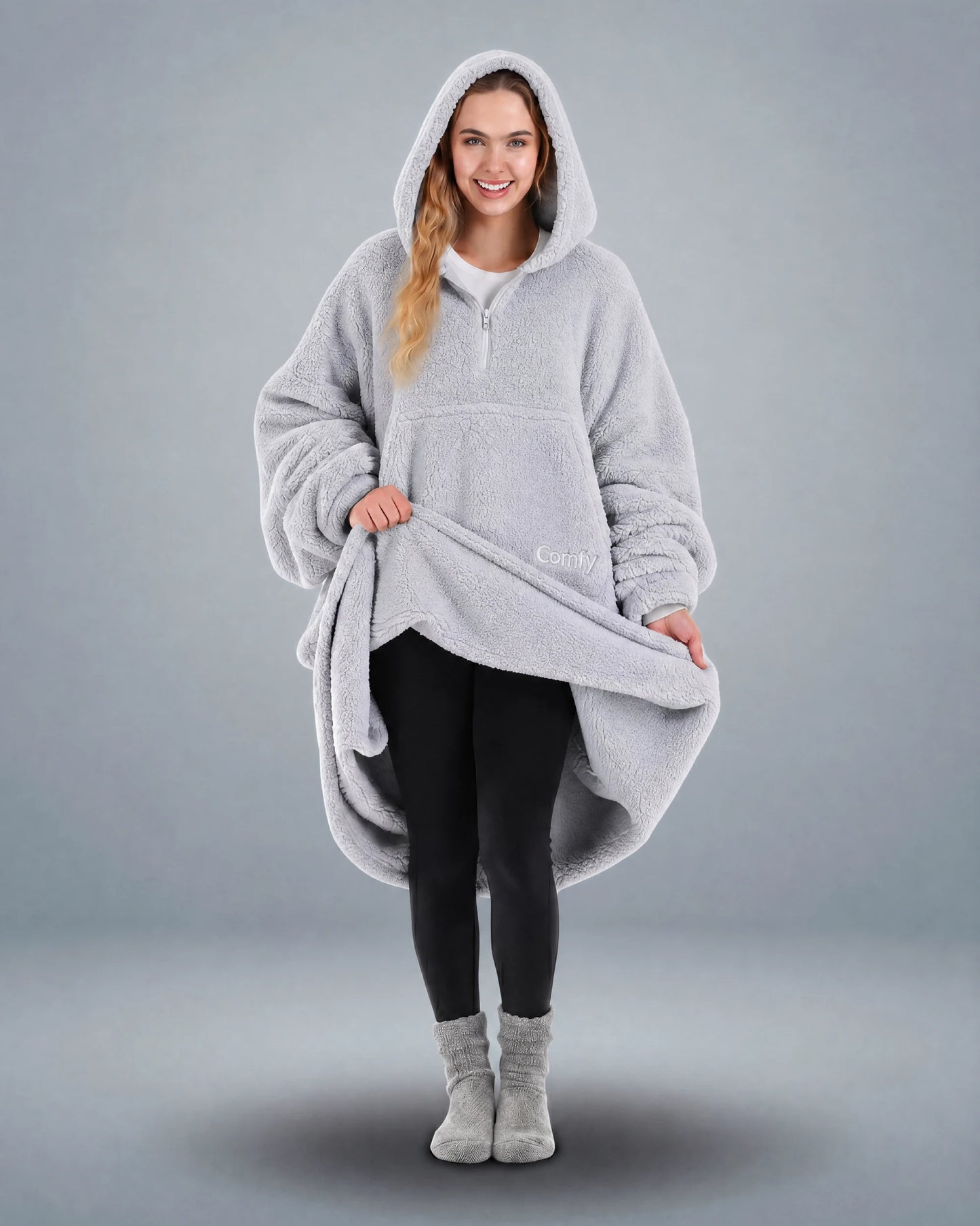 Front view of The Teddy Bear Quarter-Zip wearable blanket in light gray with model lifting hem to show full coverage and plush interior