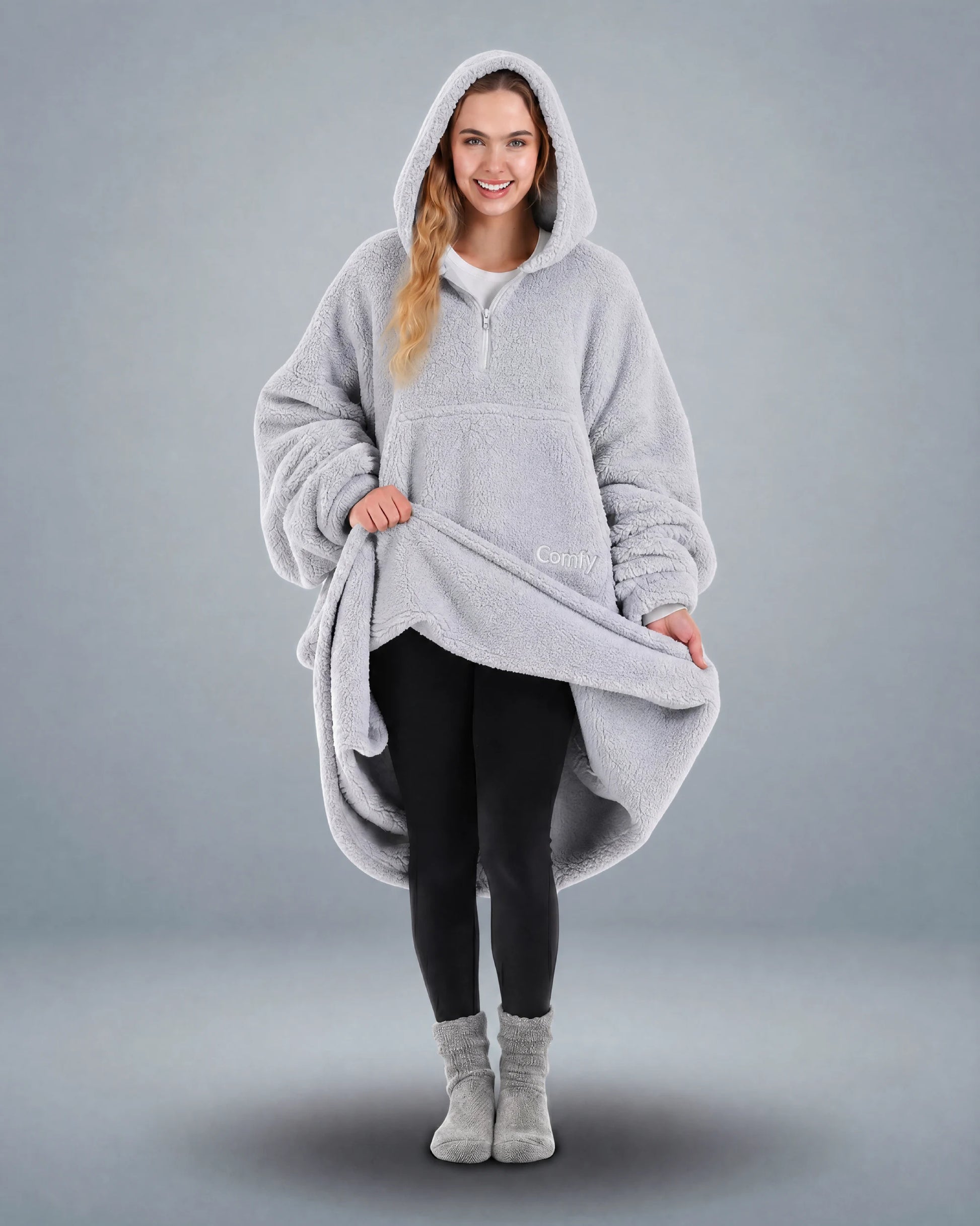 Front view of The Teddy Bear Quarter-Zip wearable blanket in light gray with model lifting hem to show full coverage and plush interior