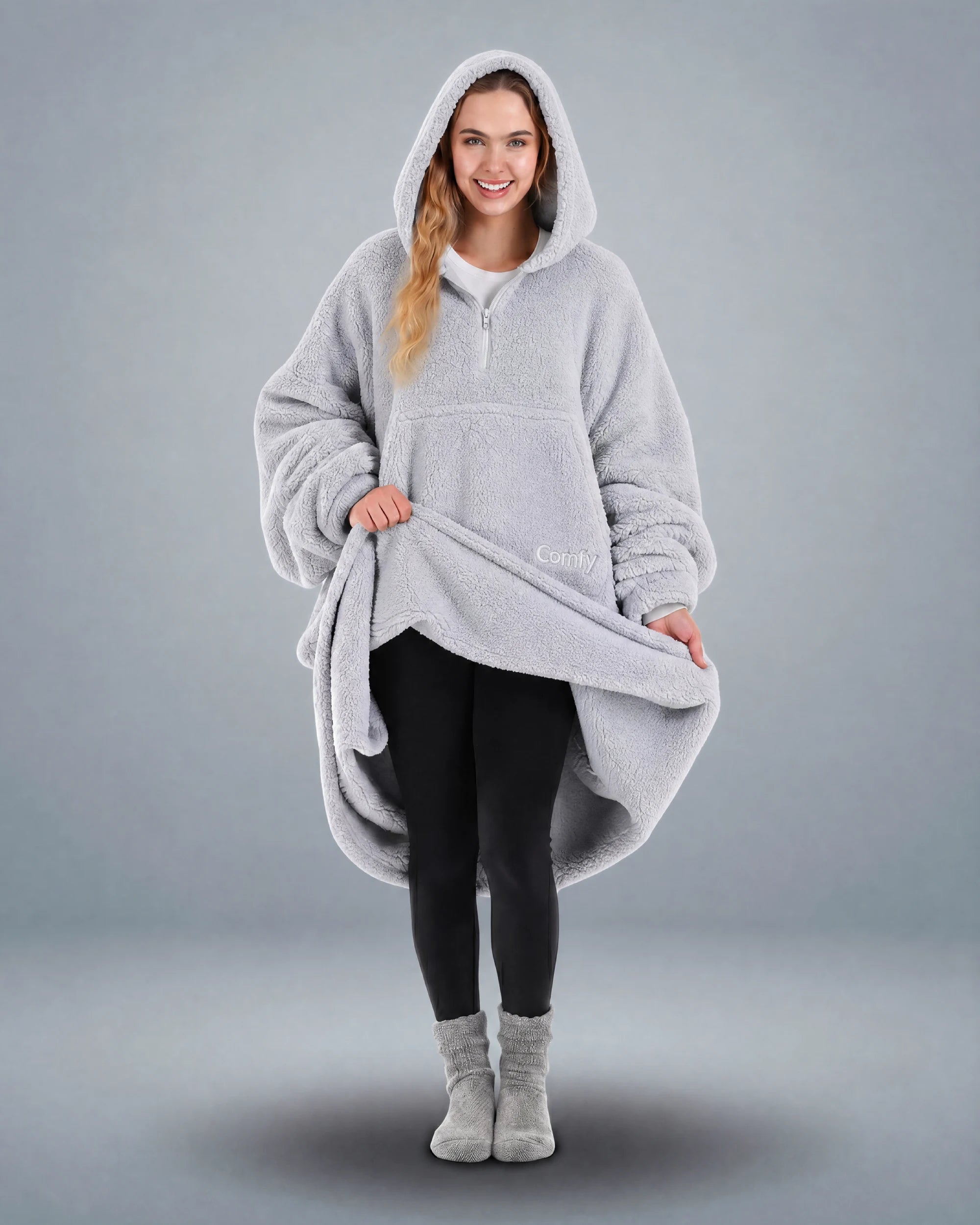 Front view of The Teddy Bear Quarter-Zip wearable blanket in light gray with model lifting hem to show full coverage and plush interior