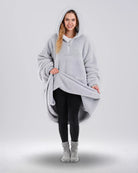 Front view of The Teddy Bear Quarter-Zip wearable blanket in light gray with model lifting hem to show full coverage and plush interior