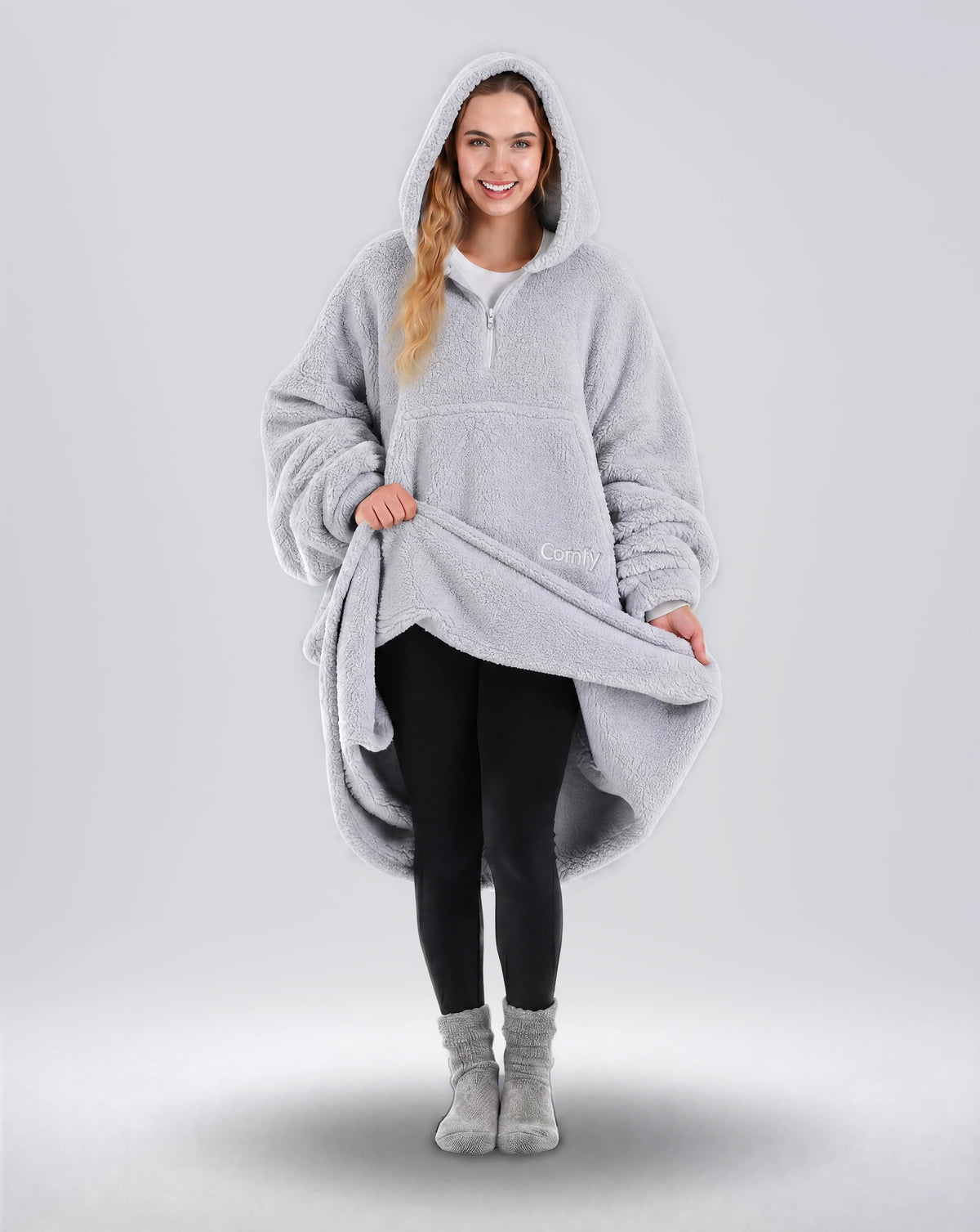 Front view of The Teddy Bear Quarter-Zip wearable blanket in light gray with model lifting hem to show full coverage and plush interior