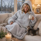 Lifestyle view of The Teddy Bear Quarter-Zip wearable blanket in light gray worn lounging on a couch with a cat and holding a mug, showing cozy at-home use