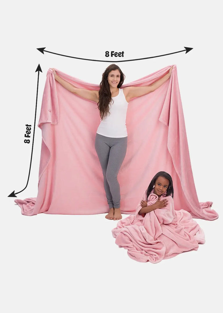 A woman holding the comfy blanket to show the size of it, and a girl sitting and wrapping herself in another the comfy blanket in pink color