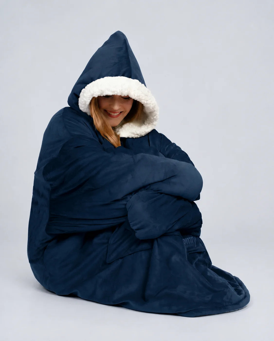 Woman sitting wrapped in The Original wearable blanket in blue showing oversized comfort and warmth
