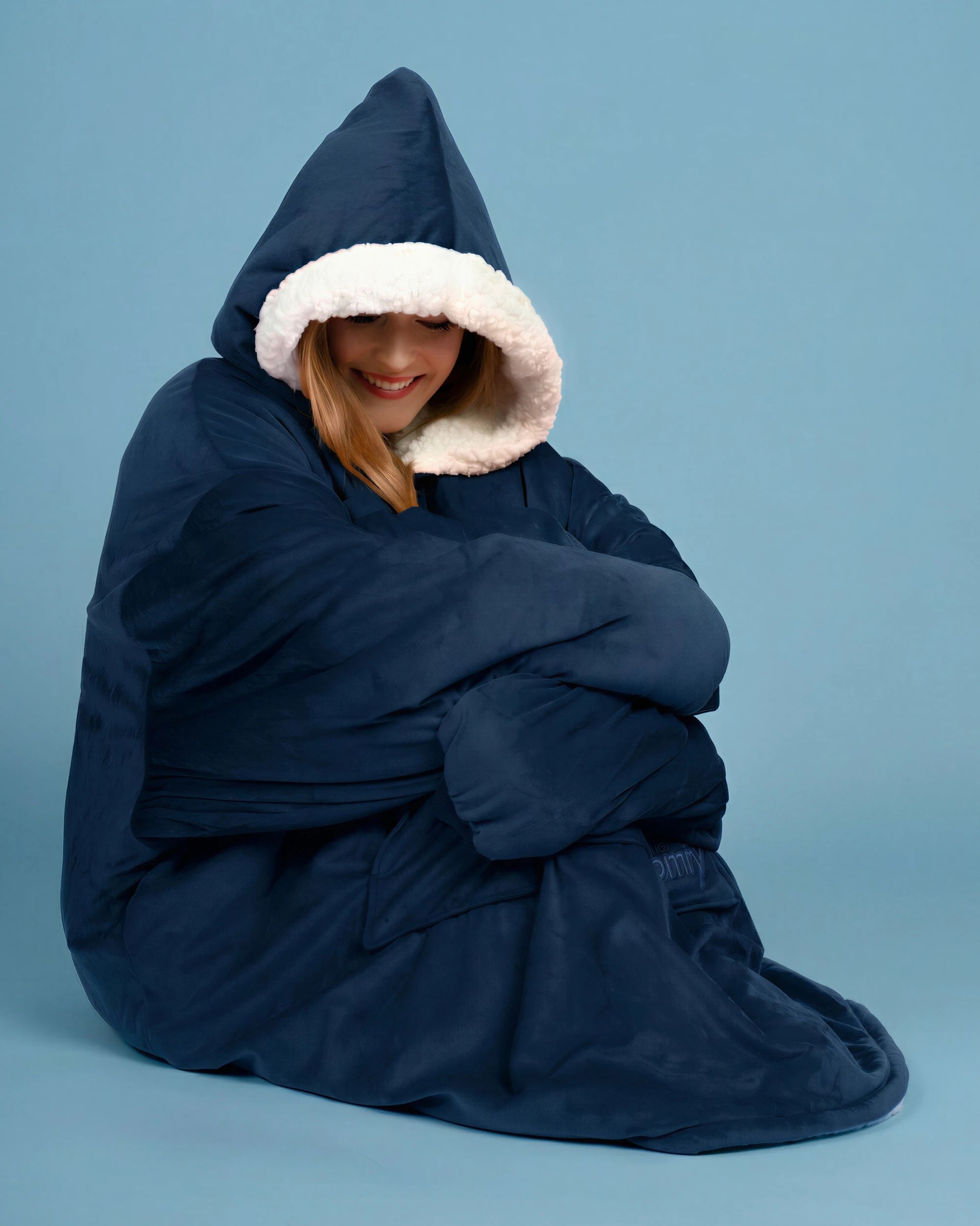 Woman sitting wrapped in The Original wearable blanket in blue showing oversized comfort and warmth