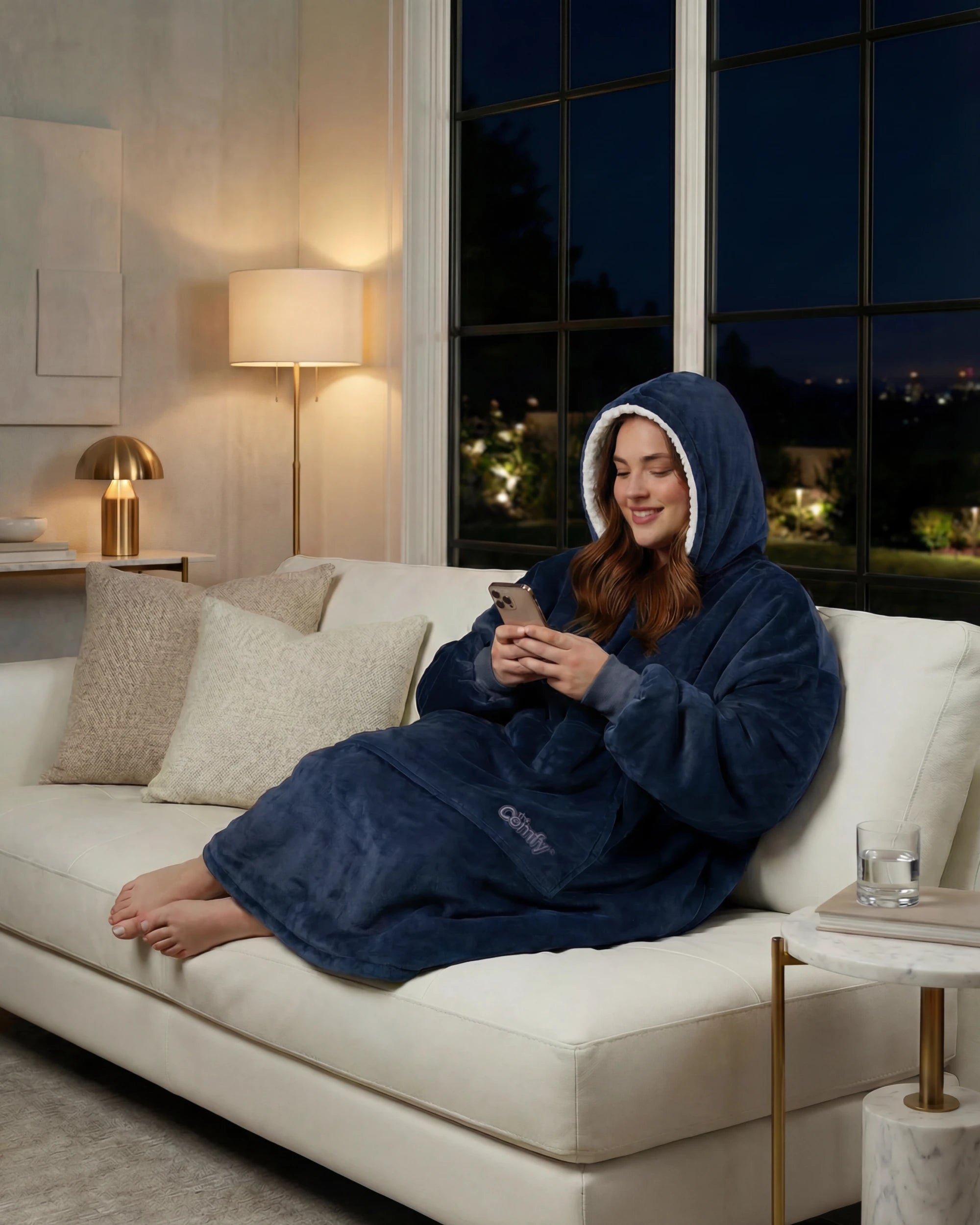 Woman wearing The Original wearable blanket in blue relaxing on a couch while using a phone