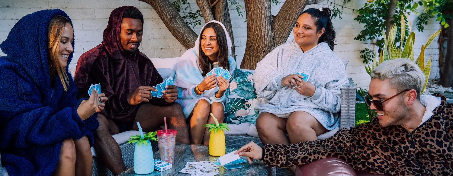 People playing cards and wearing the different wearable blankets from The Comfy